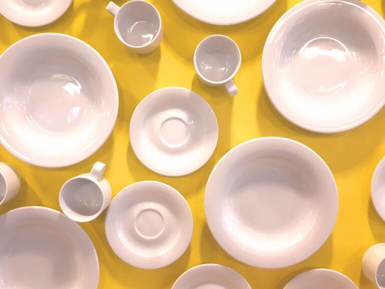 Weiße Teller und Tassen auf gelbem Untergrund