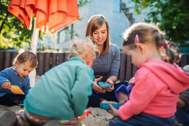 Kinderbetreuung Kita Eine junge Frau und zwei Kinder spielen draußen