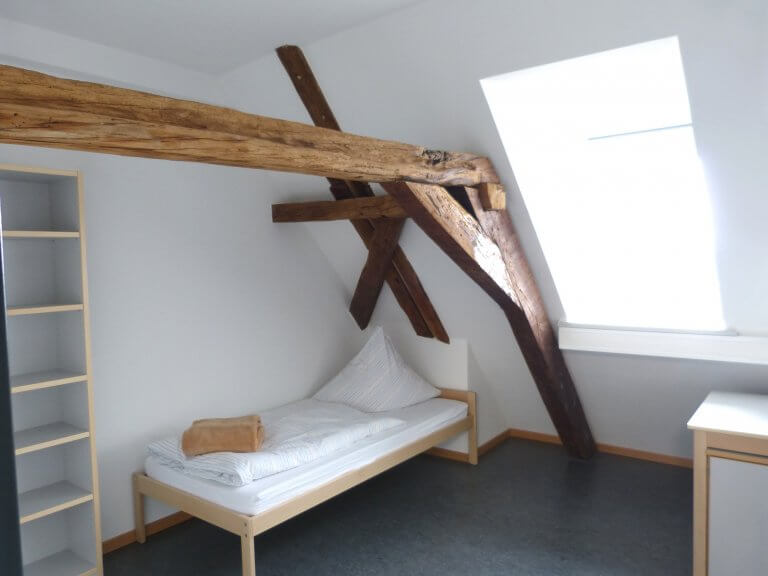 Zimmer unterm Dach in der Ritterstraße - ein deckenbalken ist freigelegt, darunter steht das Bett