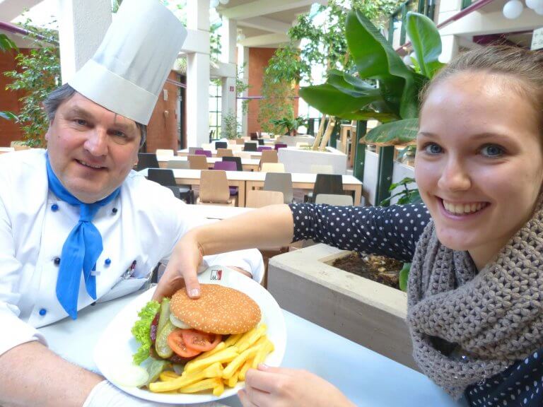 Ein Koch bietet einer jungen Frau einen Hamburger an